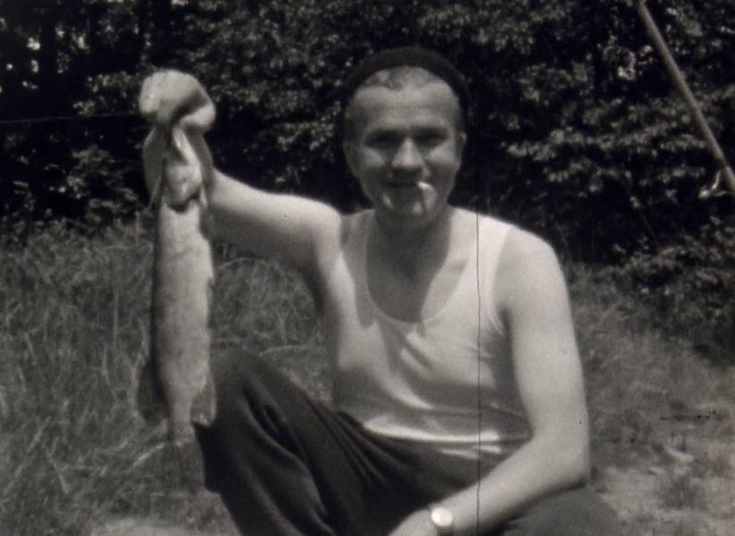 Ein Mann schaut in die Kamera. Im Mundwinkel trägt er lässig eine Zigarette. Stolz hebt er seinen gefangenen Fisch nach oben. 