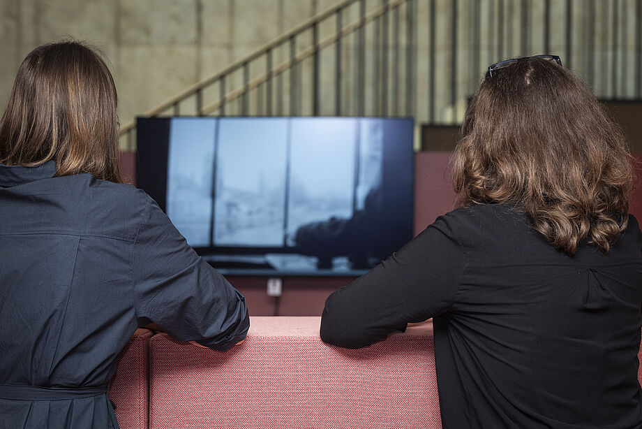 Zwei Personen schauen sich auf einem Monitor historische Filmaufnahmen an